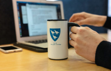 Kopp med Lierne kommune-logo, PC og hender ved skrivepult